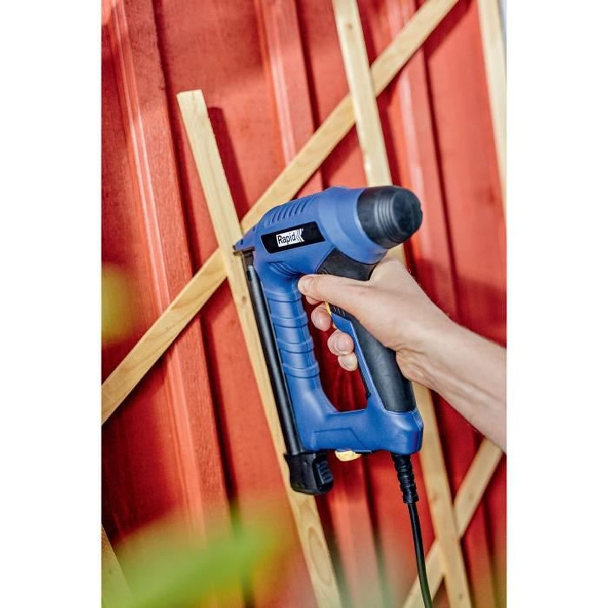 Una mano tiene una sparapunti blu per fissare doghe di legno a una parete rossa.
