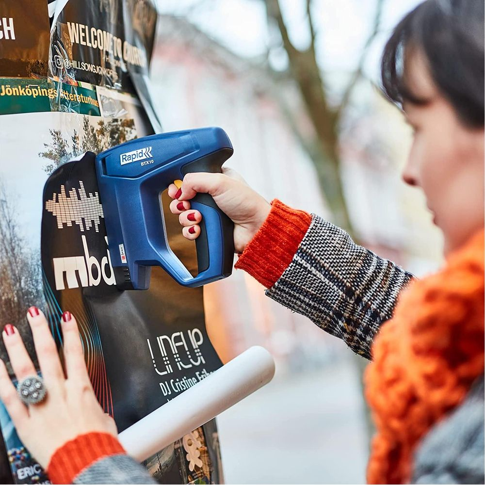 Una donna usa una sparapunti blu per attaccare un poster a un muro.