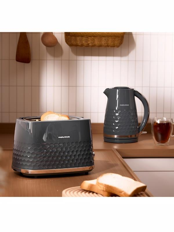 Kızarmış ekmekli gri tost makinesi, yanında su ısıtıcısı ve bir fincan çay.