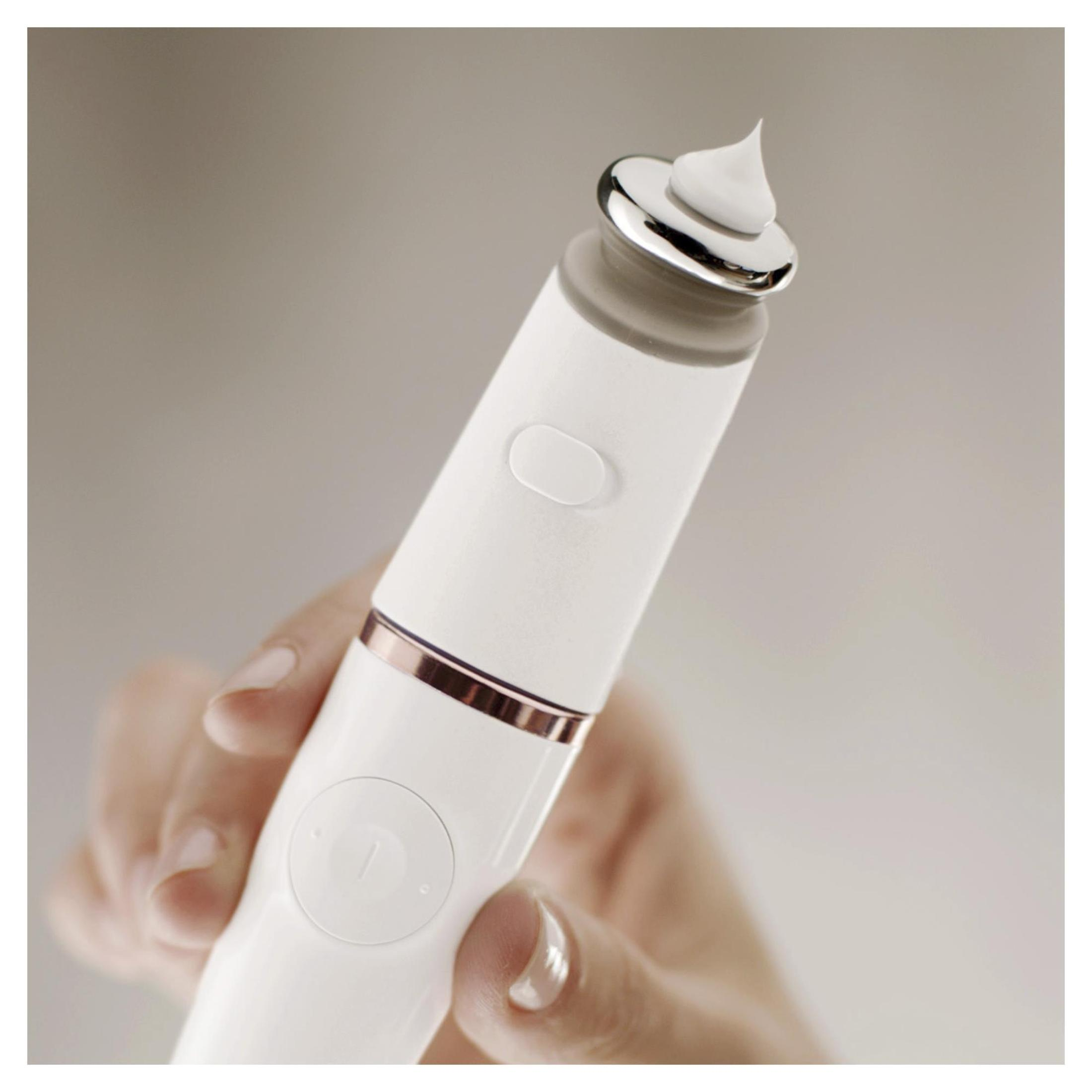 Una mano sostiene un dispositivo de cuidado de la piel blanco con punta plateada, con crema blanca encima.