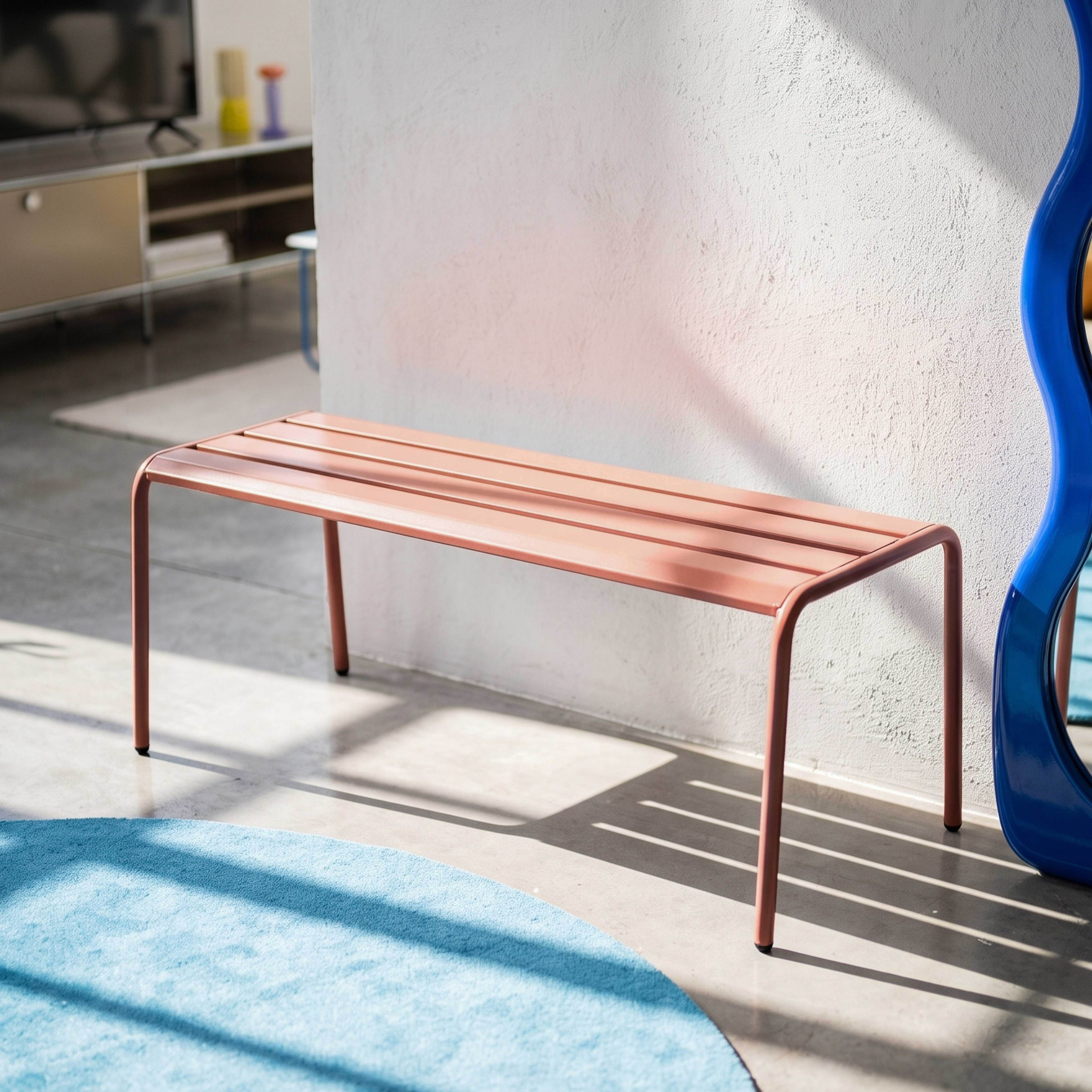 Ein rosafarbener Metallhocker steht neben einem blauen Spiegel und einer blauen Teppichrolle.