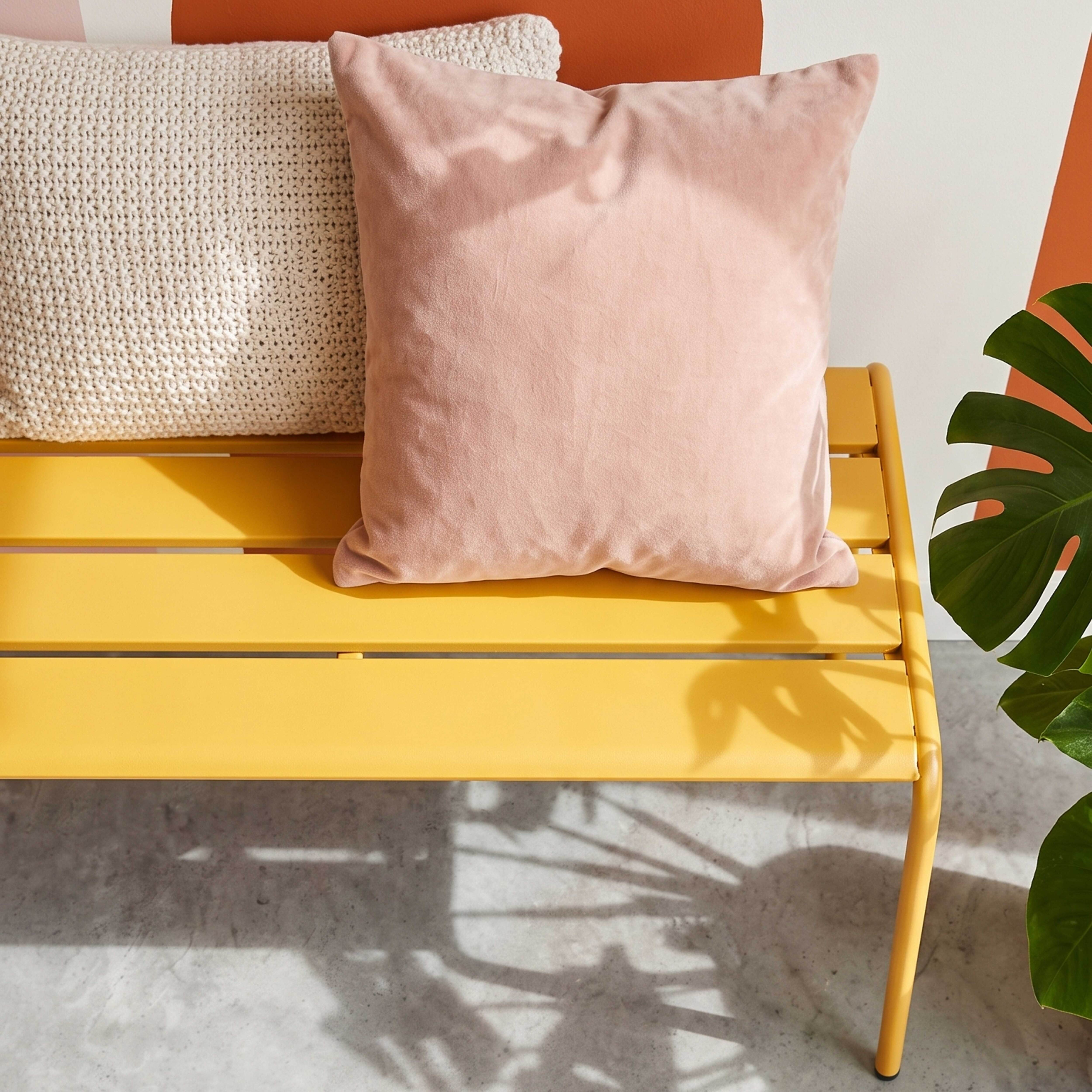 Ein gelbes Metallsofa mit zwei Kissen und einem Monstera-Blatt.