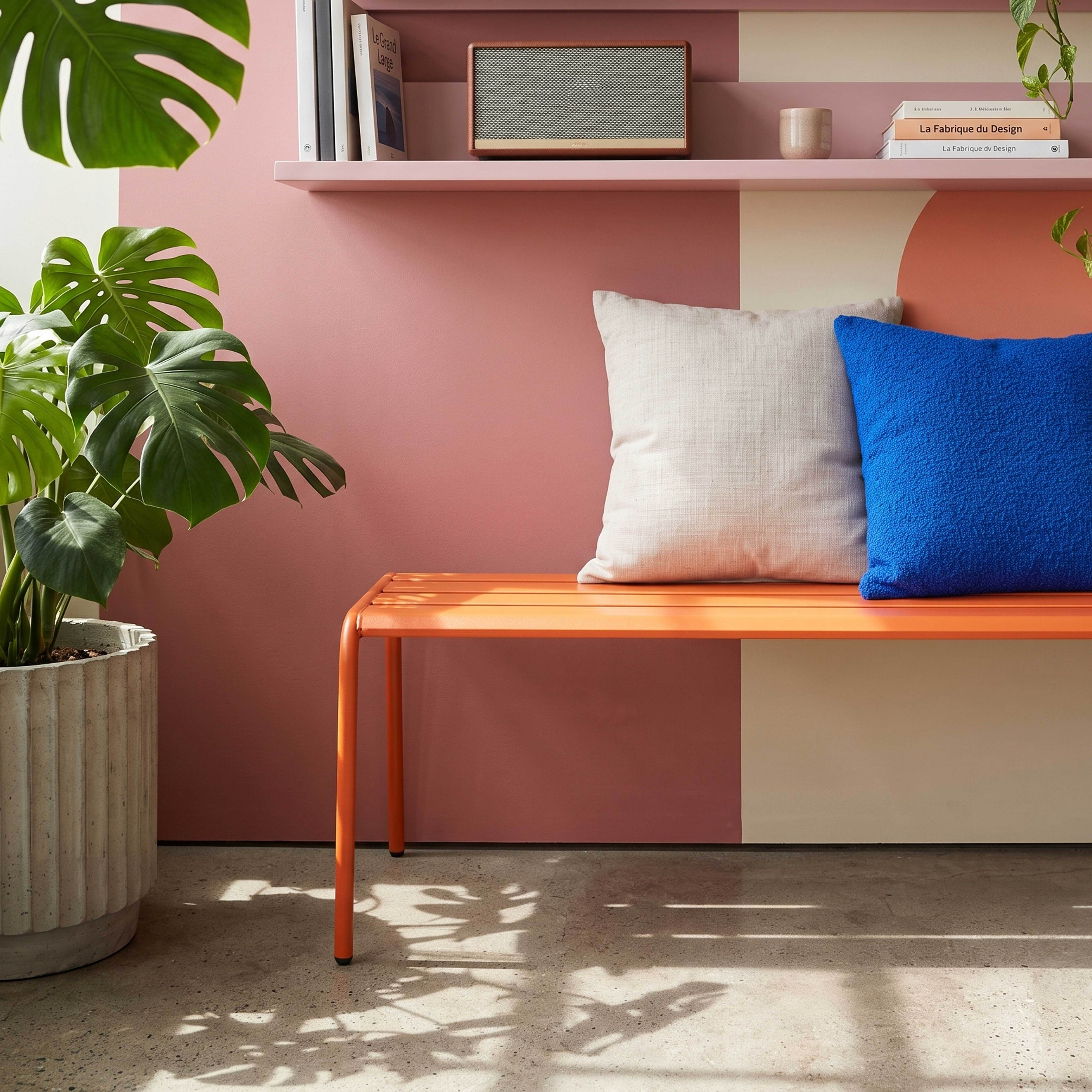 Eine orange Bank mit Kissen vor einer Wand mit rosa und cremefarbenen Feldern.