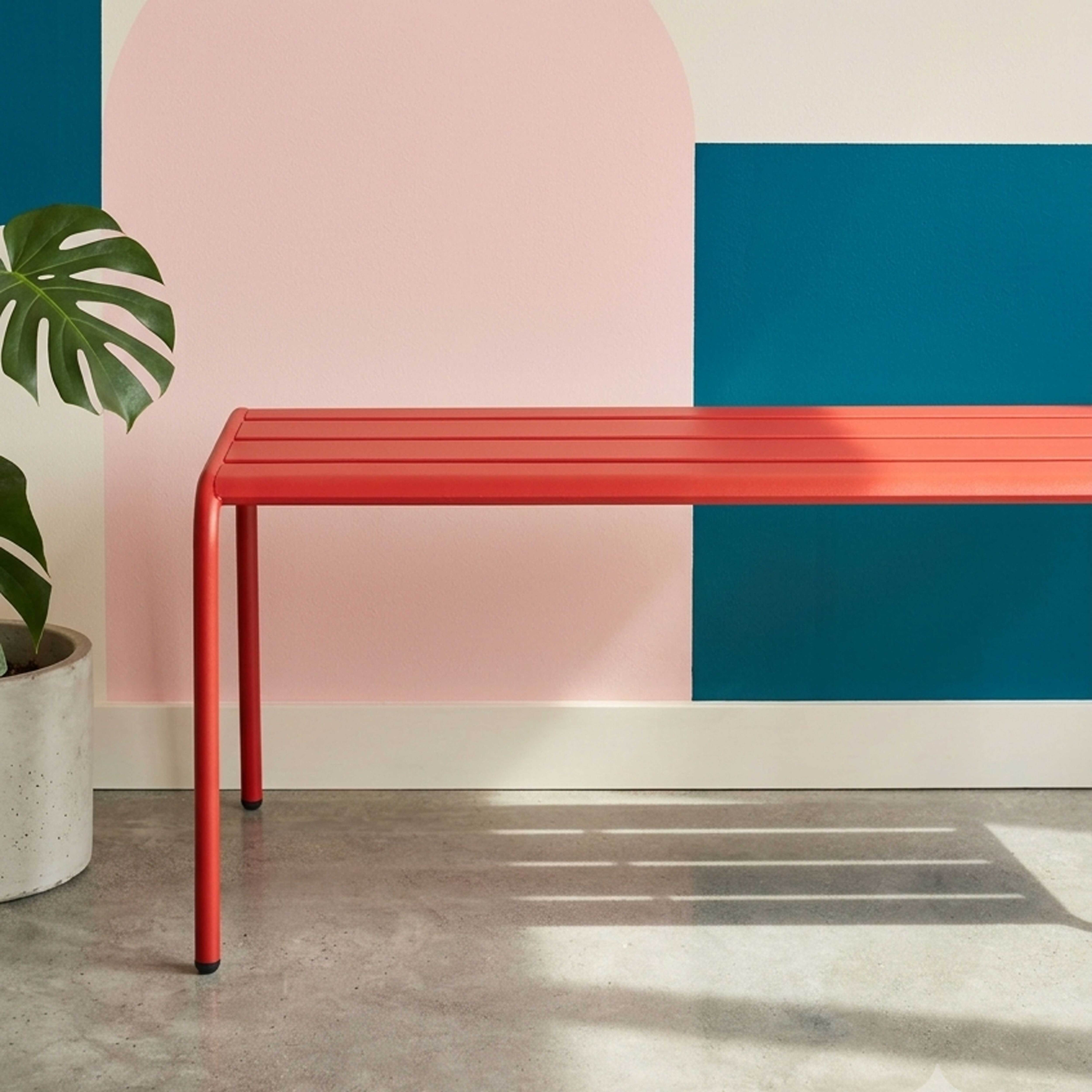 Rote Bank vor einer Wand mit rosa und blaugrünen geometrischen Formen.