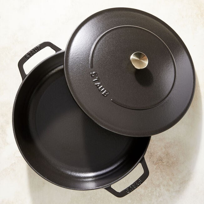 Una olla negra de hierro fundido con tapa, sobre una superficie clara.