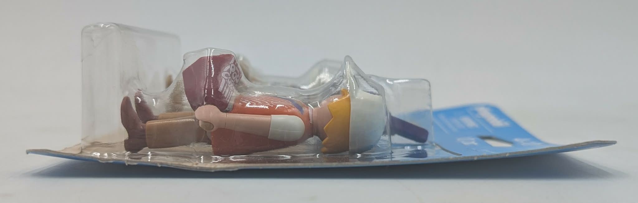 Una figura giocattolo giace in una confezione di plastica, con capelli gialli e top rosso.