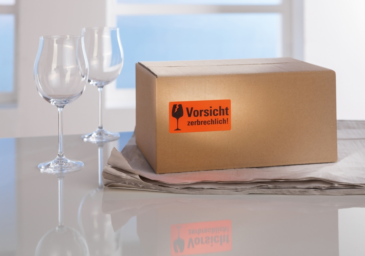 Ein Paket mit zerbrechlich-Aufkleber neben zwei Weingläsern auf einem Tisch.