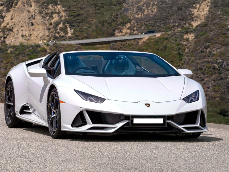 Un Lamborghini Huracán Spyder blanco aparcado en una carretera asfaltada con colinas al fondo.