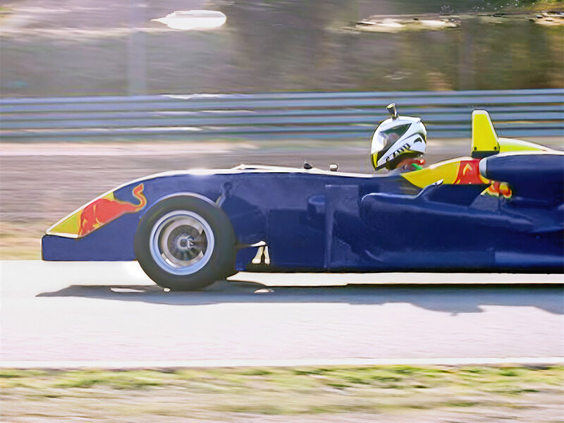 Un coche de carreras azul oscuro con detalles amarillos y rojos circula por una pista.