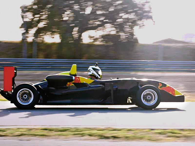 Un coche de carreras negro con detalles amarillos y rojos circula por una pista.