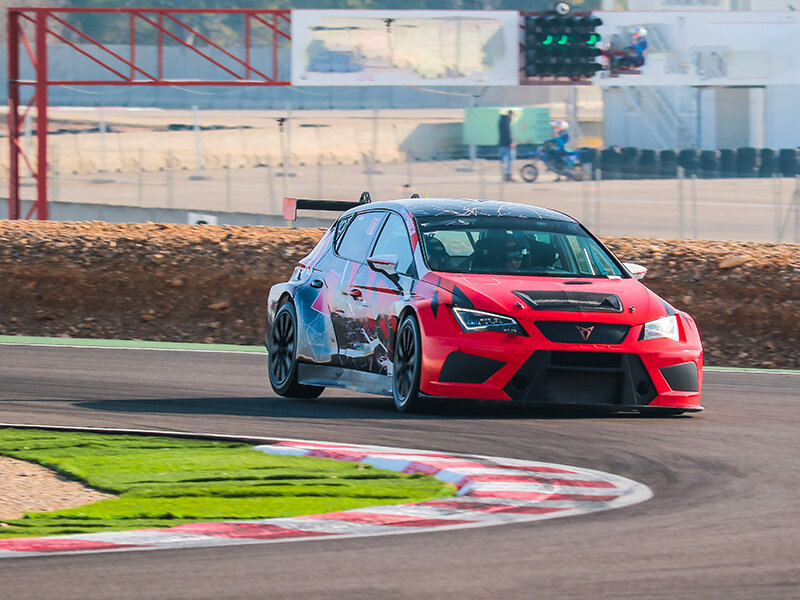 Un coche de carreras rojo con detalles negros gira en una pista con césped verde.