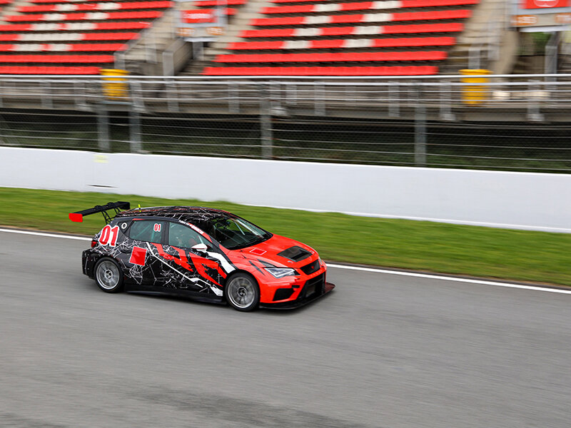 Un coche de carreras rojo y negro con el número 01 avanza en una pista.