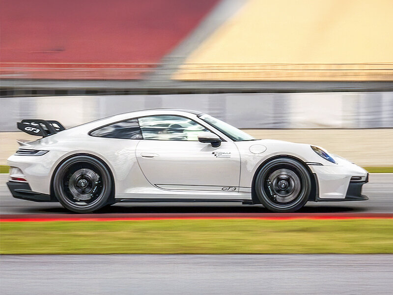Un Porsche GT3 blanco acelera en una pista, con desenfoque de movimiento en neumáticos y fondo.