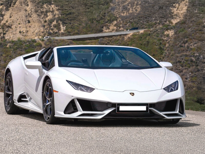 Un Lamborghini Huracán Spyder blanco aparcado en una carretera asfaltada con colinas al fondo.