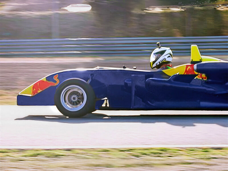 Un coche de carreras azul y amarillo con logo de toro corre en una pista. Conductor con casco.
