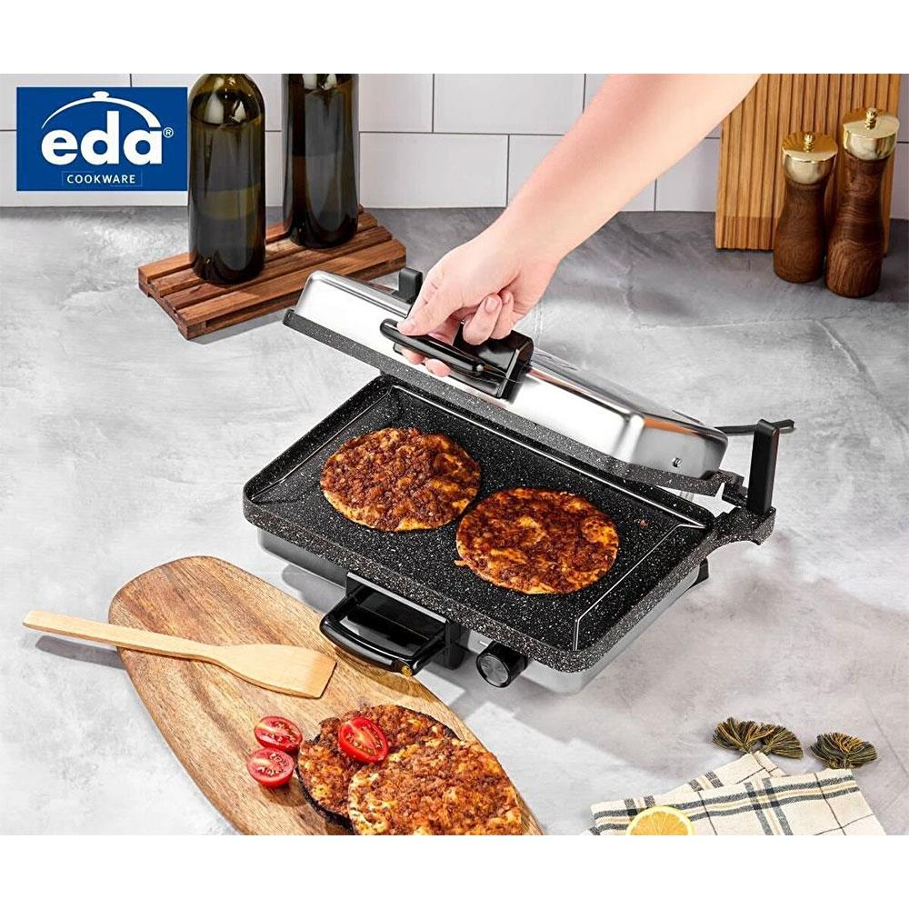 Bir el, iki burgerli bir ızgarayı açıyor. Ahşap tahtada başka bir burger ve domates.