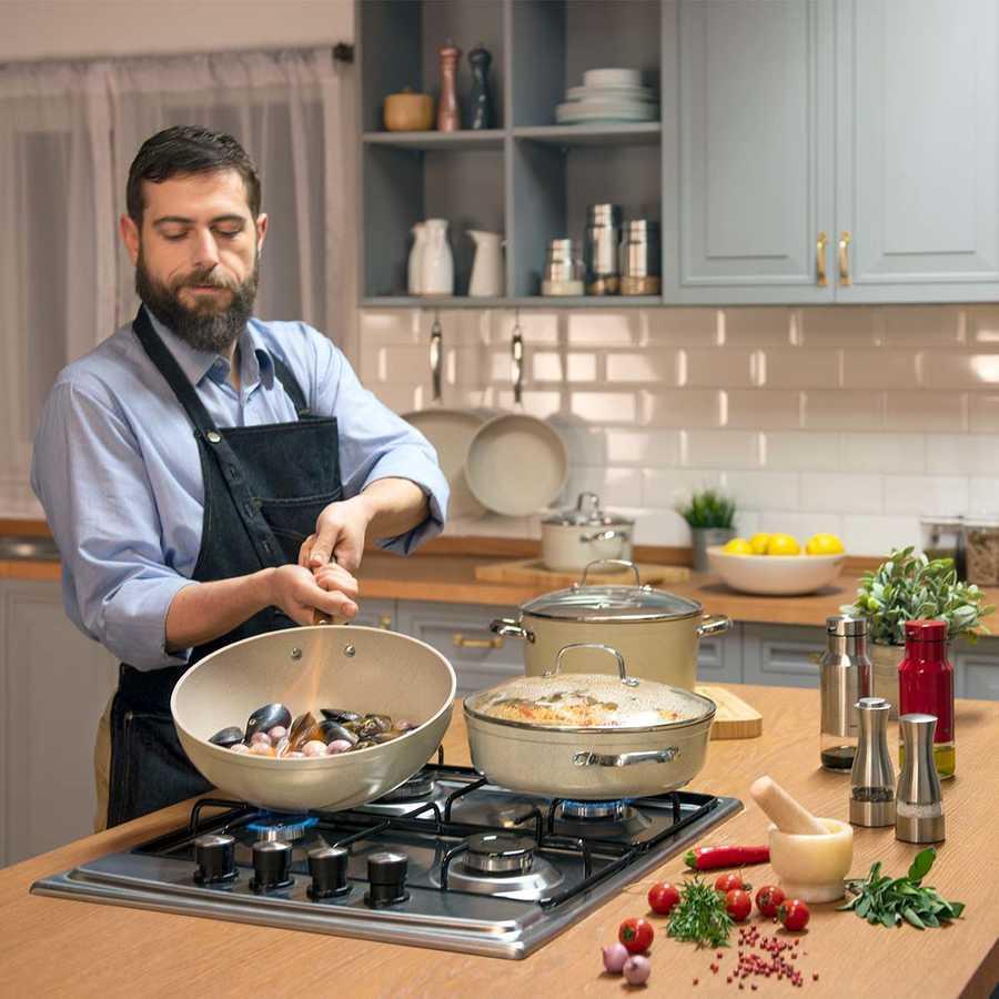 Sakallı, önlüklü bir adam gazlı ocakta tavada midye pişiriyor.