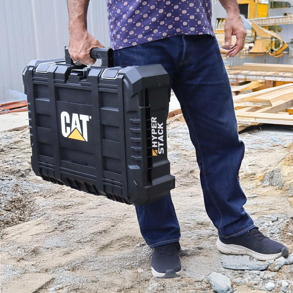 Kot pantolonlu adam inşaatta siyah CAT Hyper Stack alet çantası taşıyor.