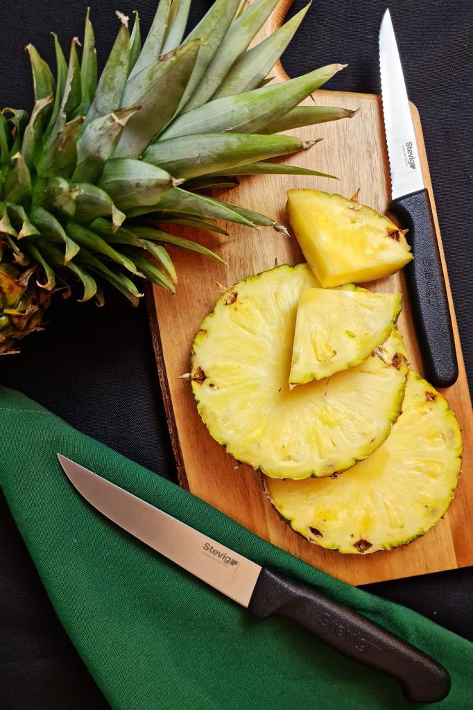 İki bıçakla tahta üzerinde kesilmiş bir ananas.