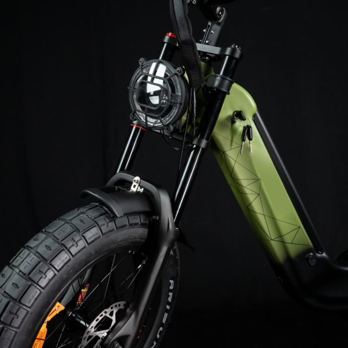 Nahaufnahme eines grünen E-Bikes mit schwarzem Rahmen, rundem Scheinwerfer und grobstolligen Reifen.
