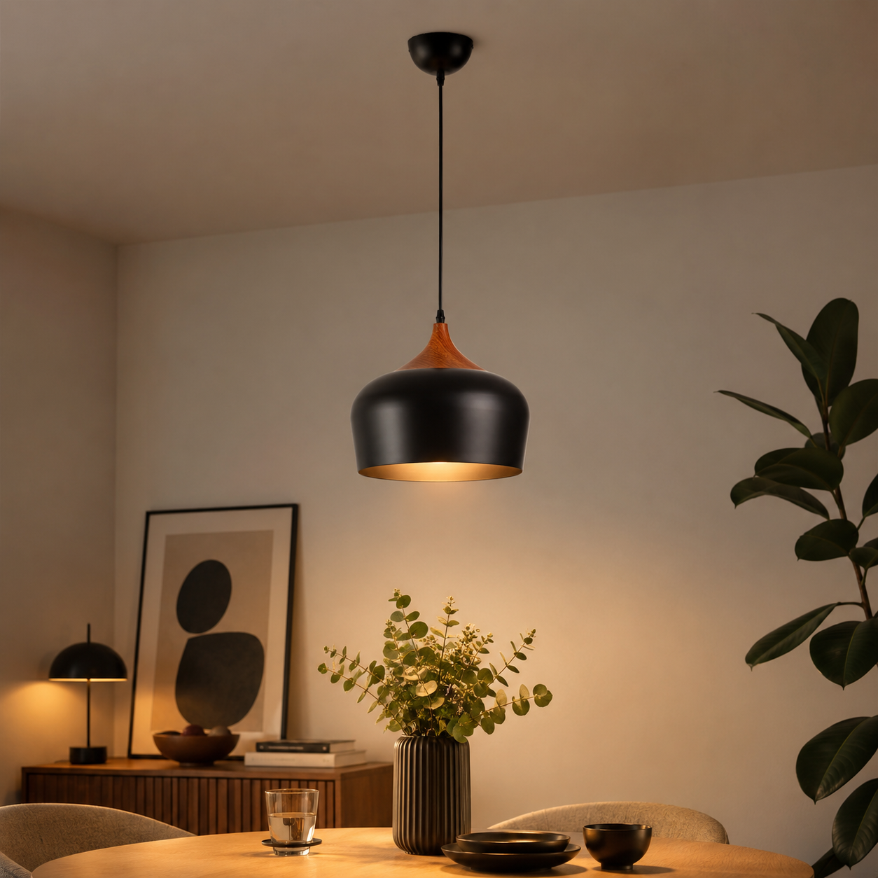 Una lámpara colgante negra con acento de madera sobre una mesa de madera con flores y platos.