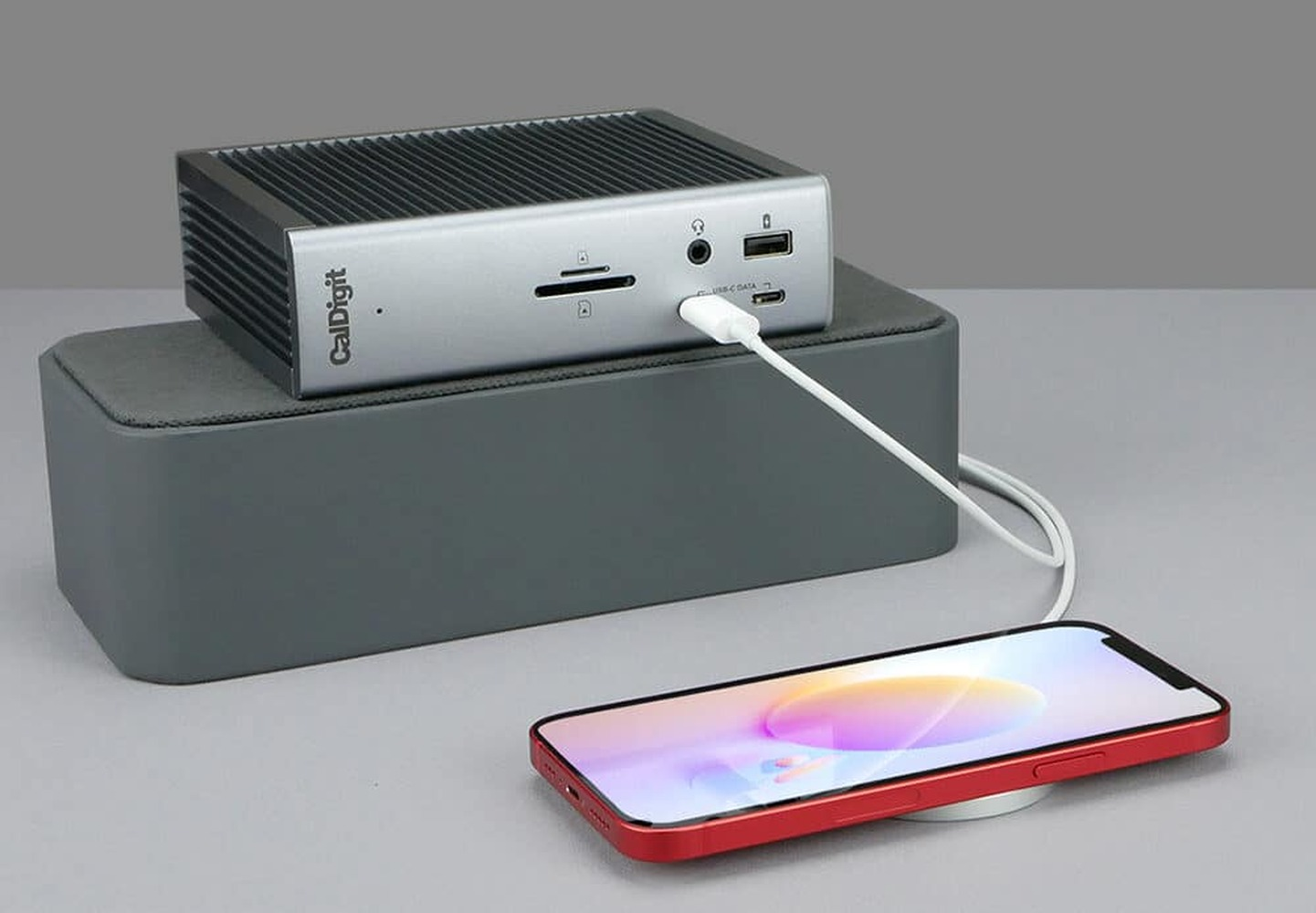 A silver CalDigit hub with SD card slots and USB ports charges a red iPhone.