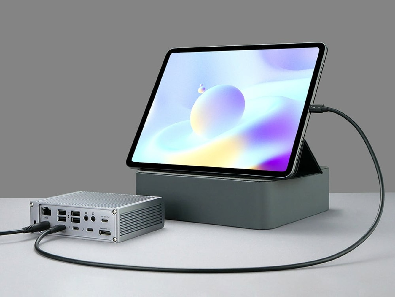 A silver docking hub with ports next to a tablet on a stand.