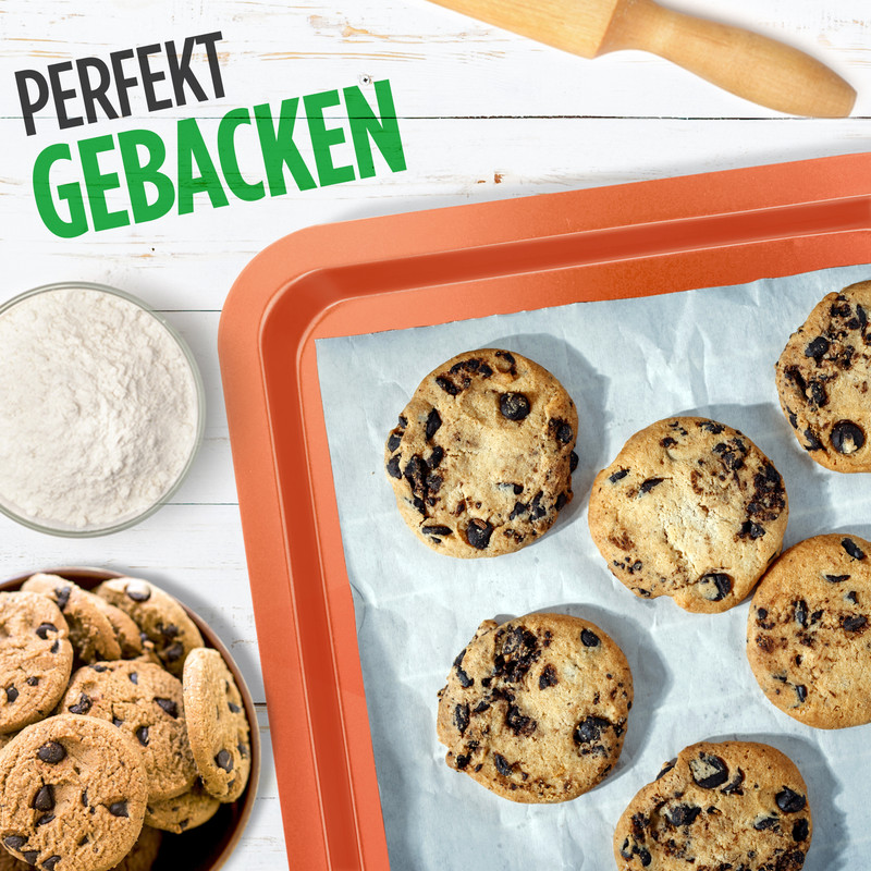 Schokoladenkekse auf einem Backblech mit einer Schüssel Mehl und einem Nudelholz.