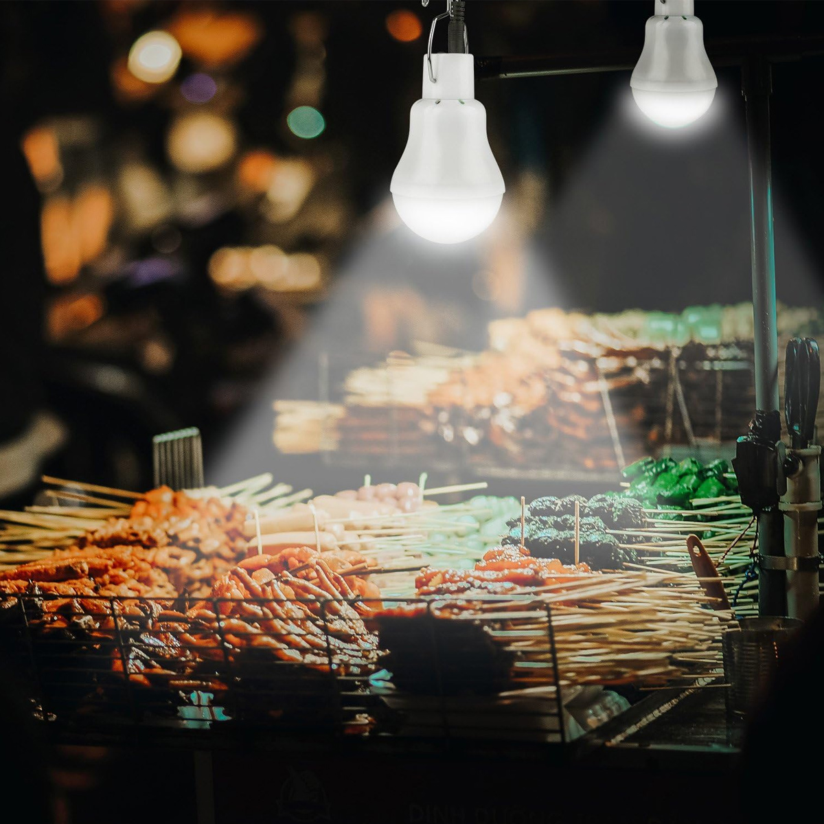 Essensstand bei Nacht mit Fleisch- und Gemüsespießen unter hellen LED-Lichtern.