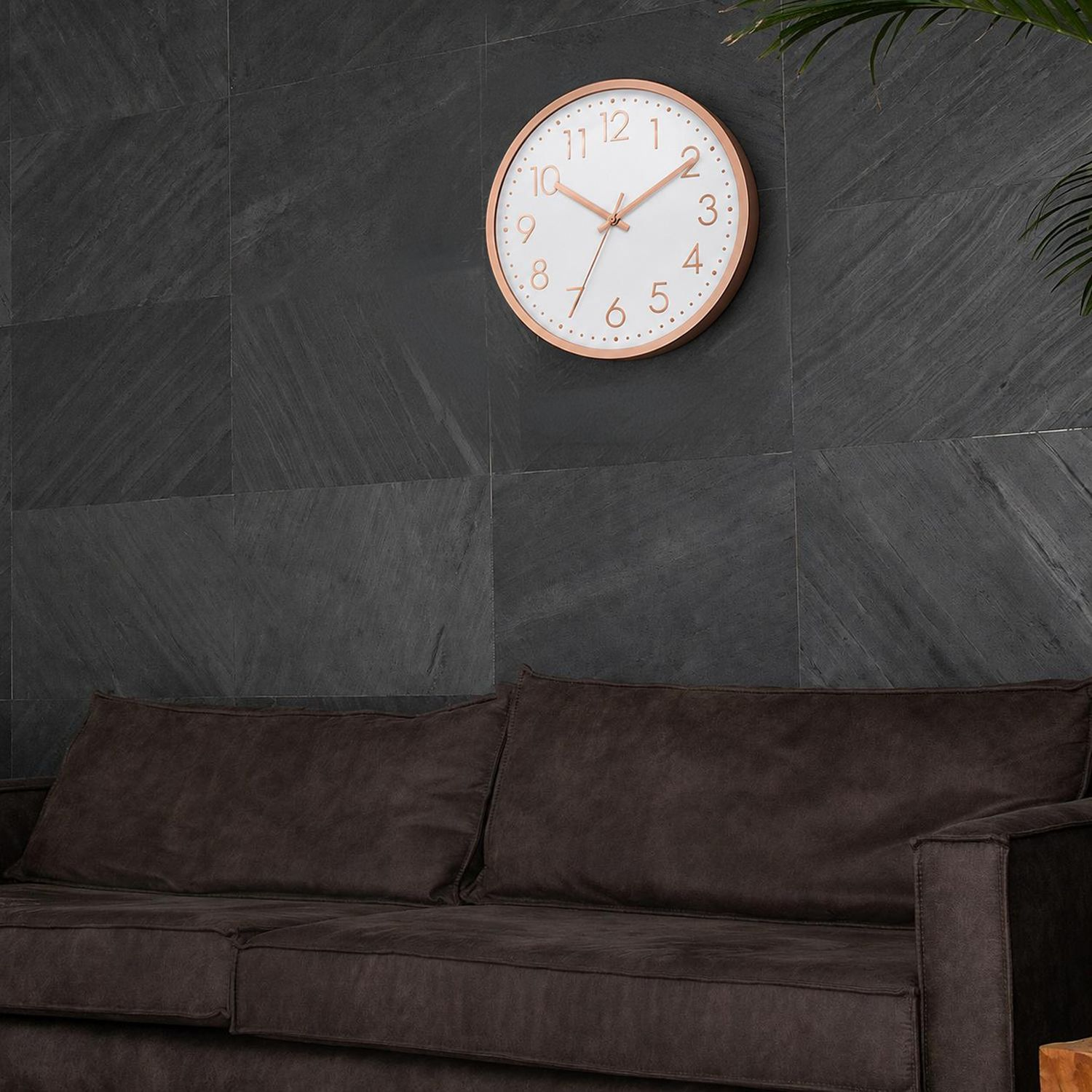 Eine runde Wanduhr mit goldenem Rahmen hängt über einem braunen Sofa.
