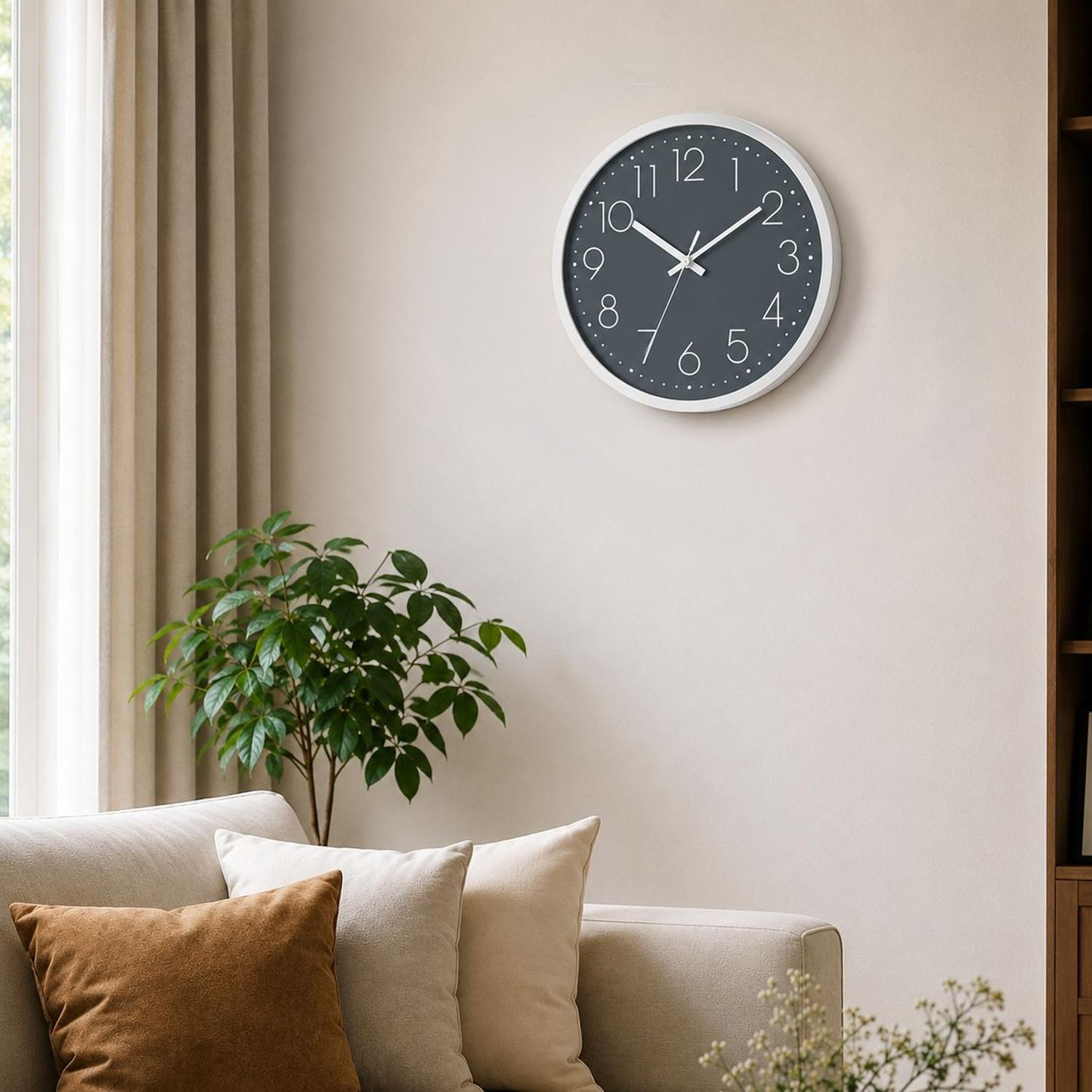 Eine Wanduhr mit dunklem Zifferblatt und weißen Zeigern hängt über einem Sofa mit Kissen.