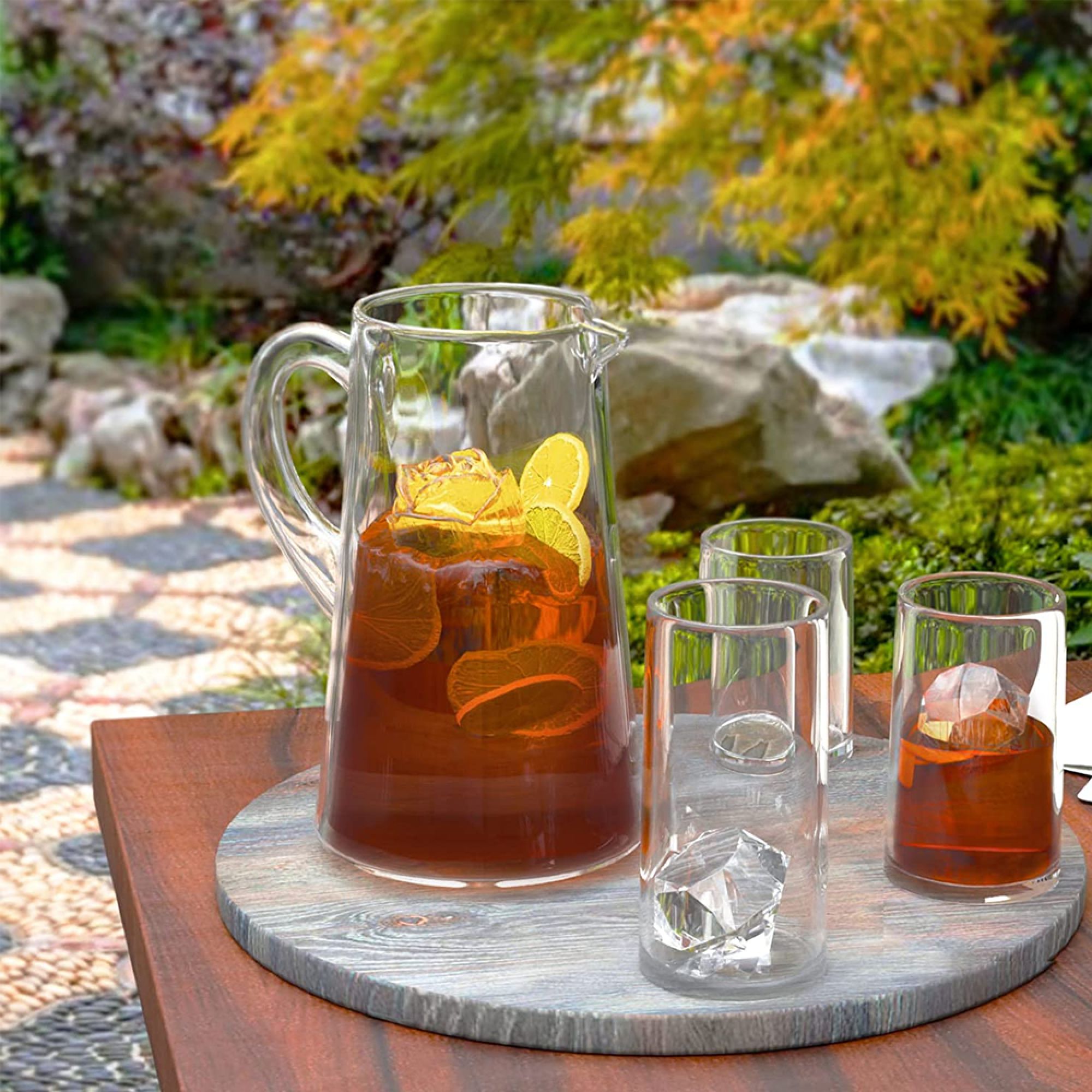 Ein Glaskrug und Gläser mit Eis und Orangenscheiben auf einem Holztisch.