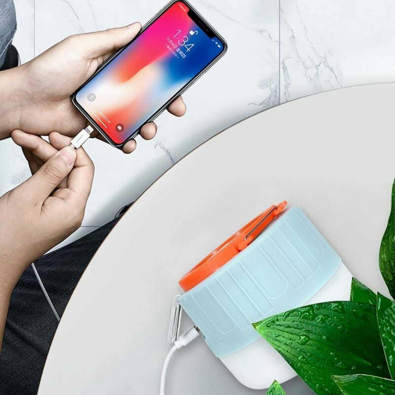 Eine Hand steckt ein Ladekabel in ein Smartphone. Daneben ein blauer Behälter.