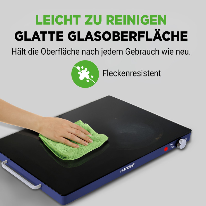 Eine Hand reinigt eine glatte schwarze Kochplatte mit einem grünen Tuch.