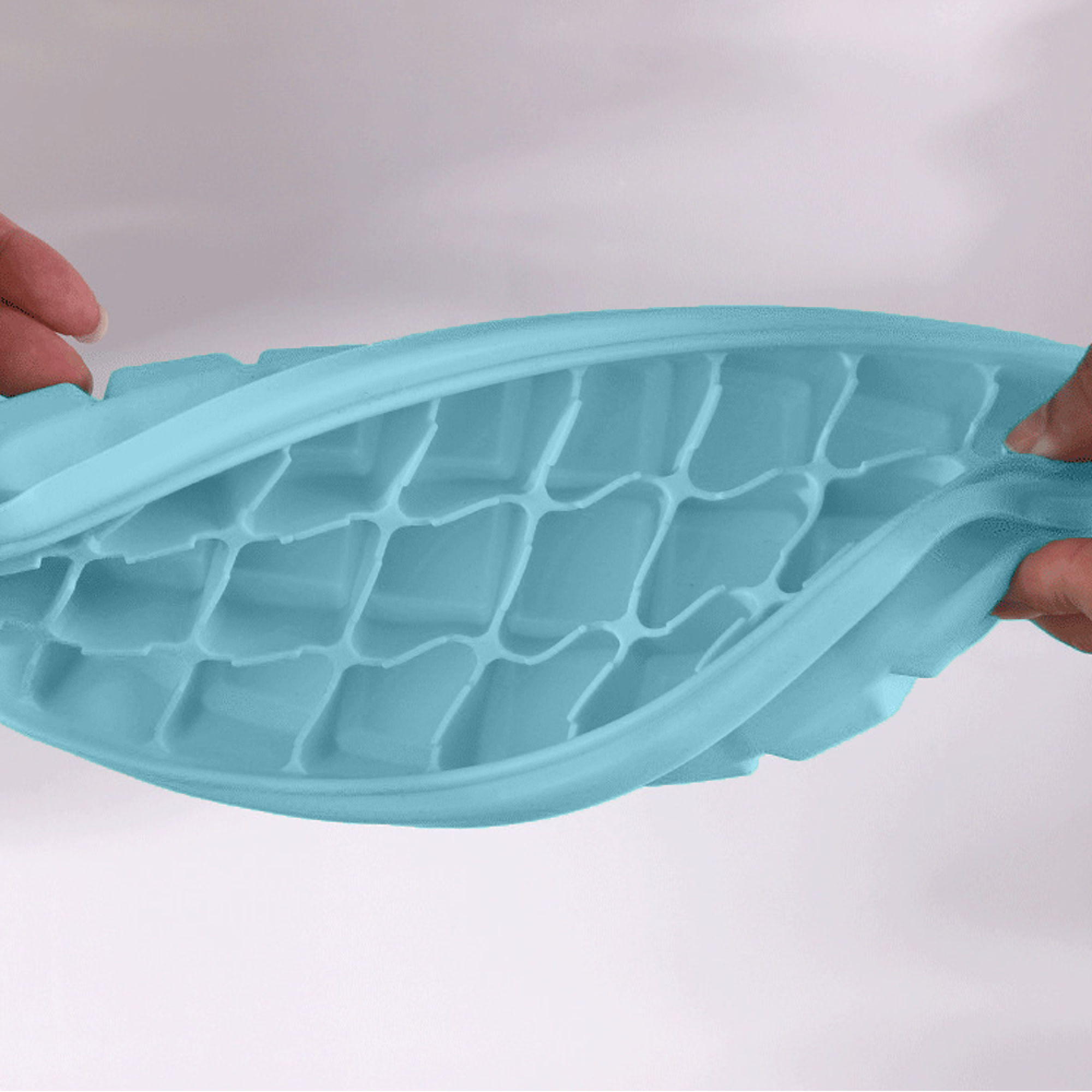 Eine hellblaue, flexible Eiswürfelform wird von Händen gehalten und gebogen.