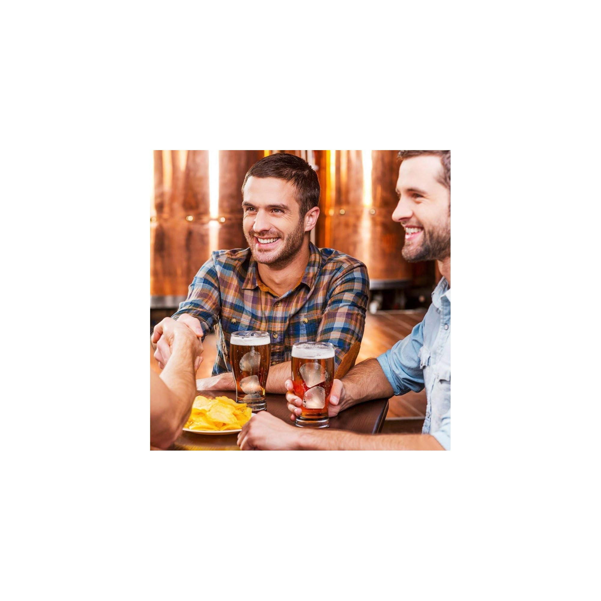 Zwei Männer schütteln sich die Hände über Biergläser und Chips in einer Brauerei.