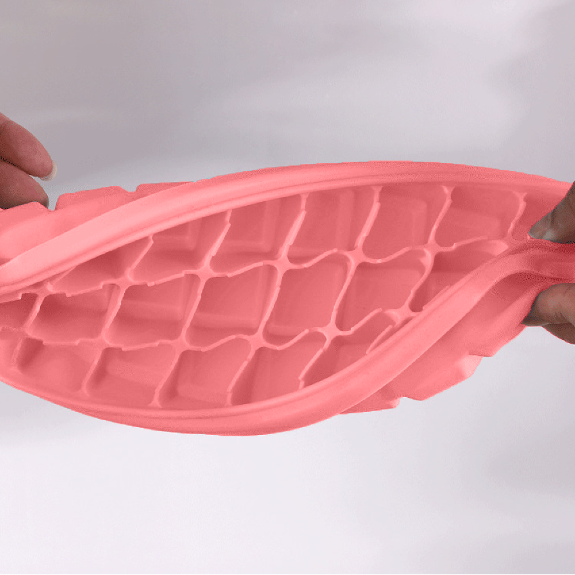 Eine rosafarbene, flexible Eiswürfelform wird von zwei Händen gehalten und gebogen.
