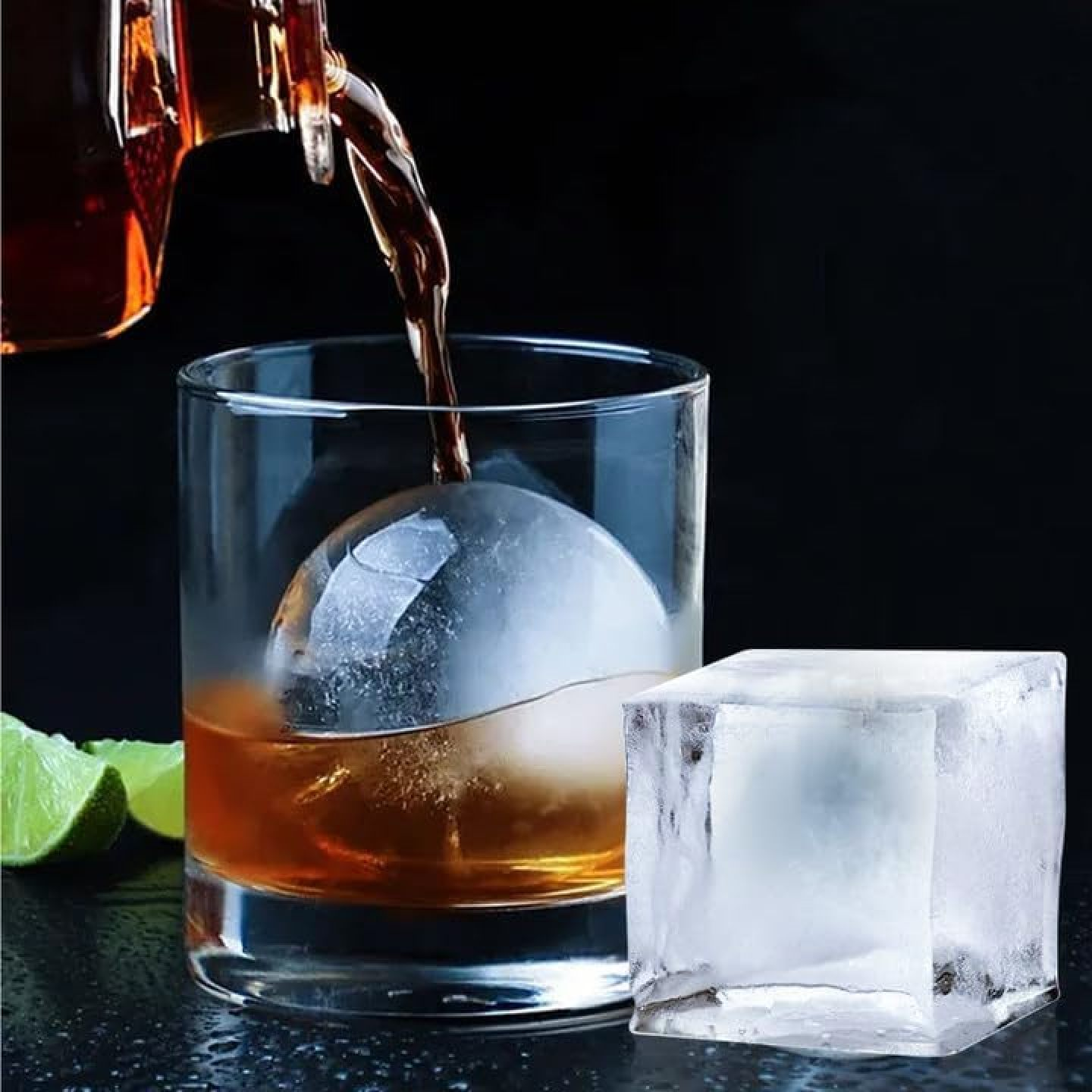Whisky wird in ein Glas mit einem großen Eisball gegossen. Ein Eiswürfel liegt daneben.