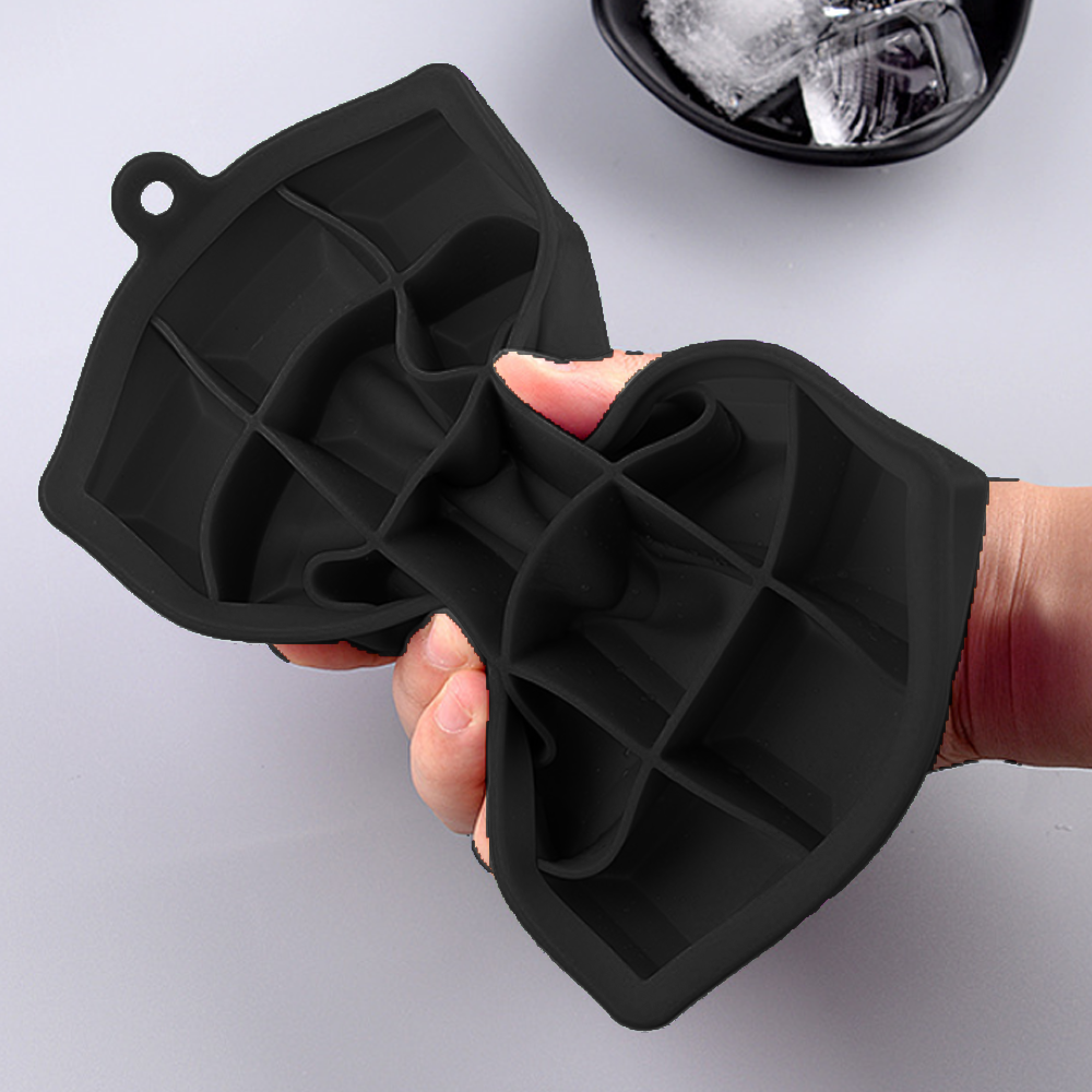 Eine Hand hält eine schwarze Silikon-Eiswürfelform mit mehreren Fächern.