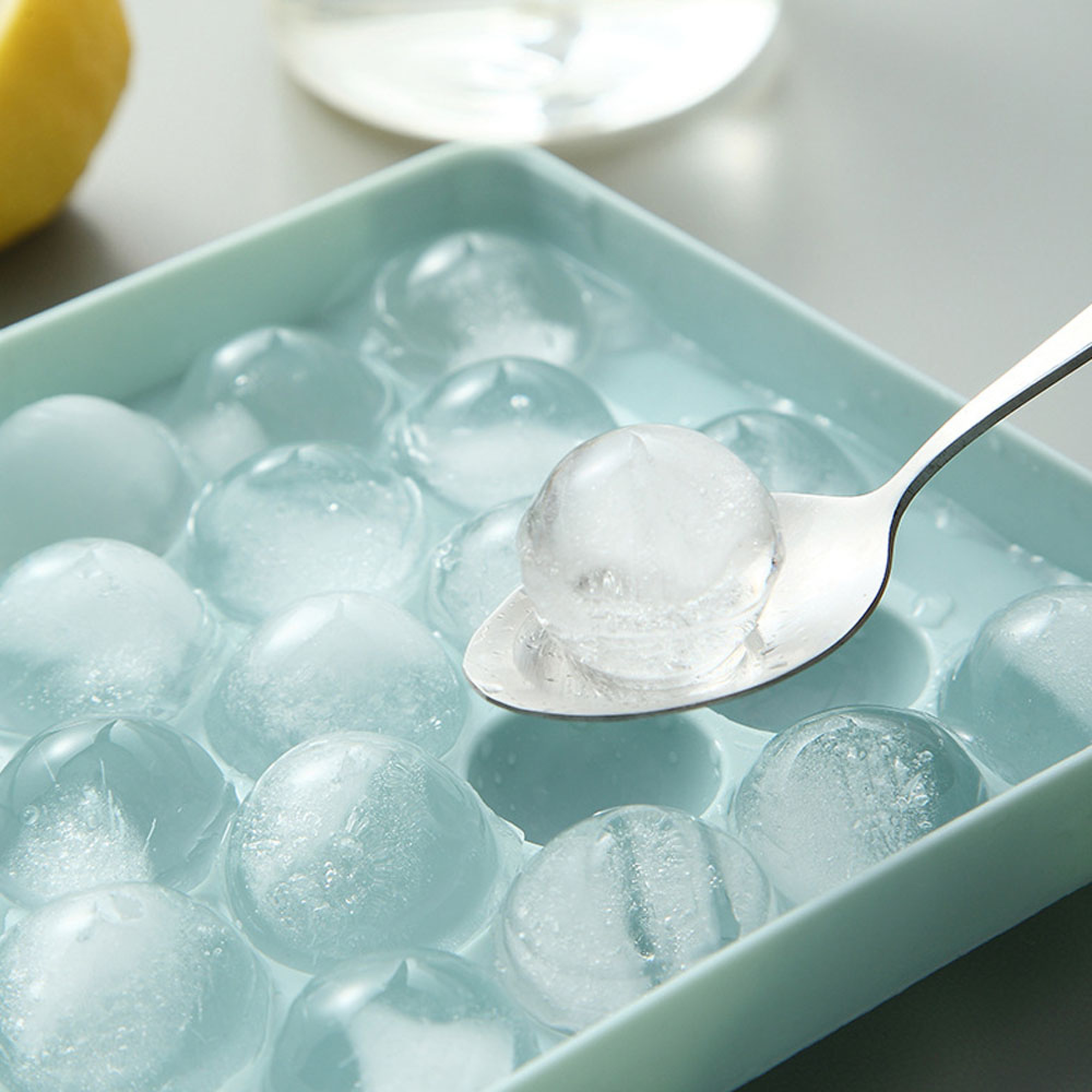 Ein Löffel hebt eine Eiskugel aus einer hellblauen Form mit vielen Eiskugeln.