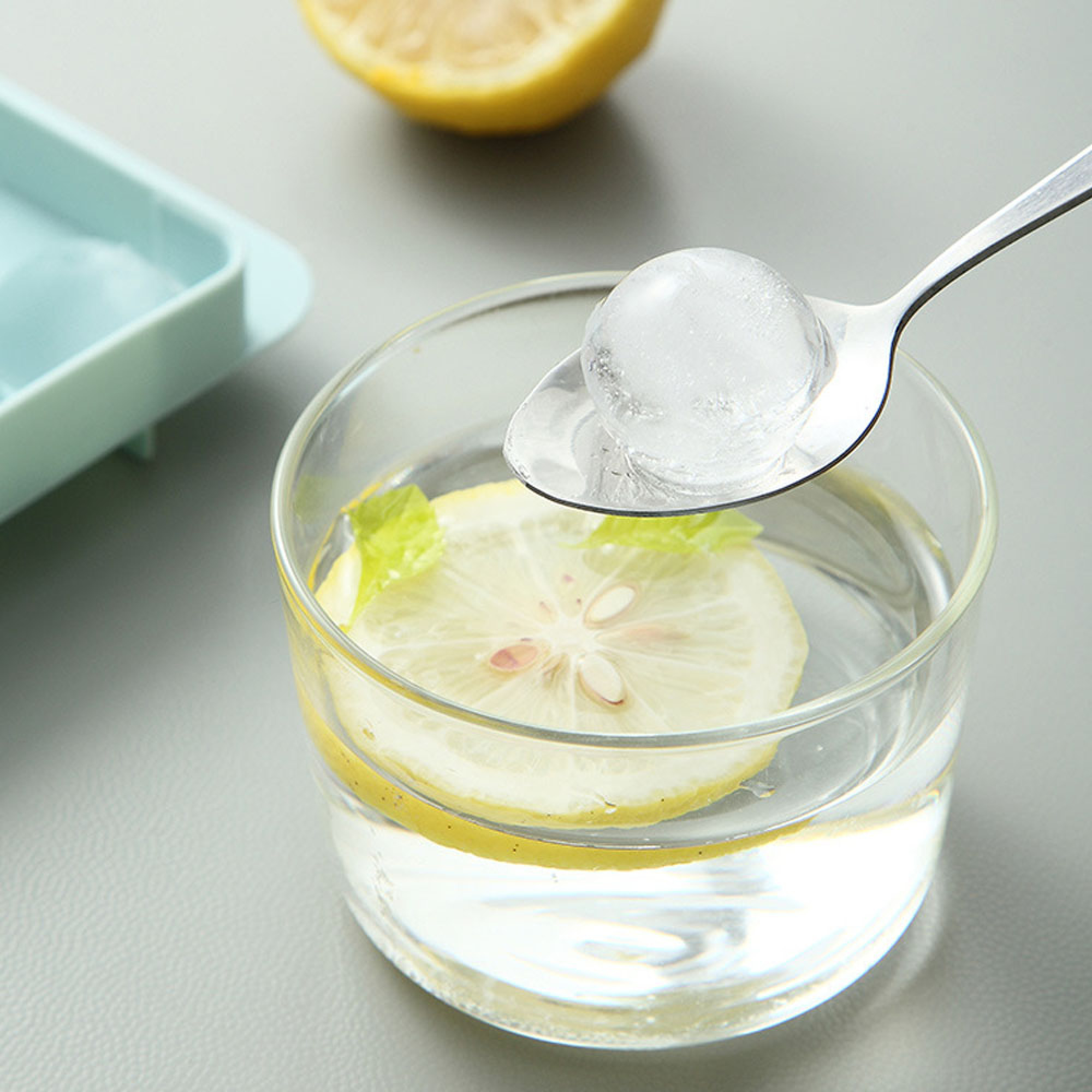 Ein Löffel mit einem Eiswürfel über einem Glas Wasser mit Zitronenscheiben.