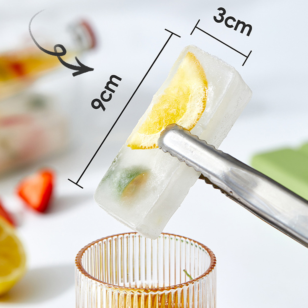 Eine Zange hält einen Eiswürfel mit Fruchtstücken über einem Glas. Maße 9x3cm.
