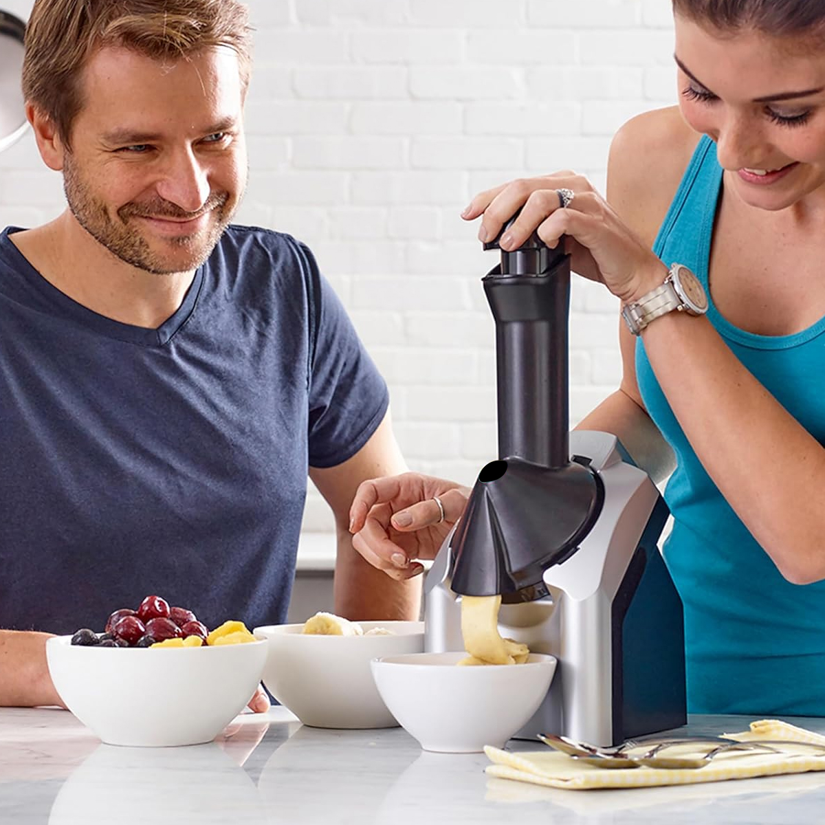 Mann und Frau machen Eis mit einer Eismaschine und Obst in Schalen.