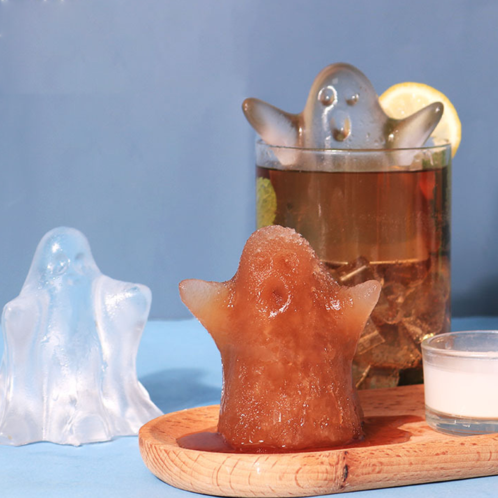 Geisterförmige Eiswürfel in einem Glas und auf einem Holzbrett.