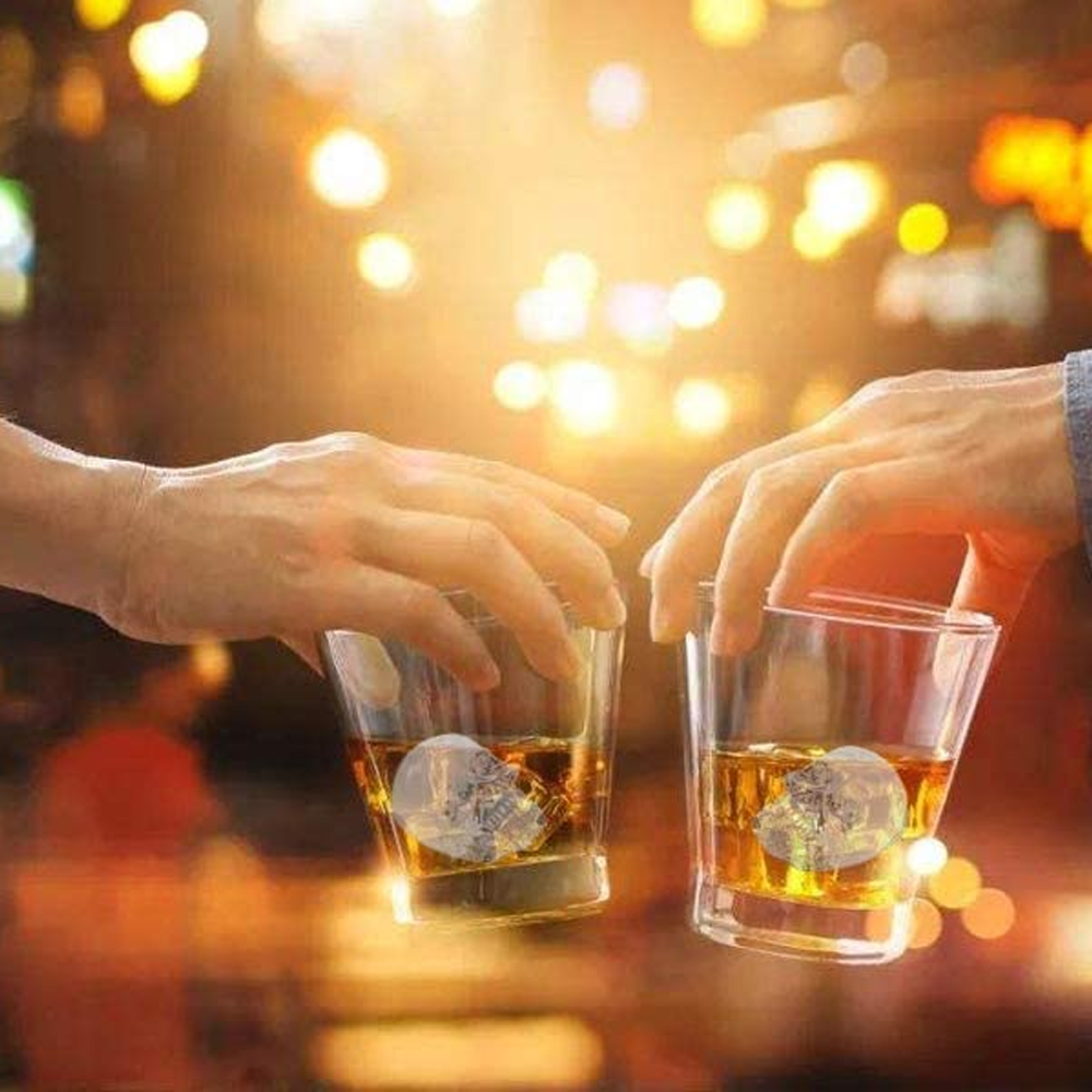 Zwei Hände halten Gläser mit Whisky und Totenkopf-Eiswürfeln.