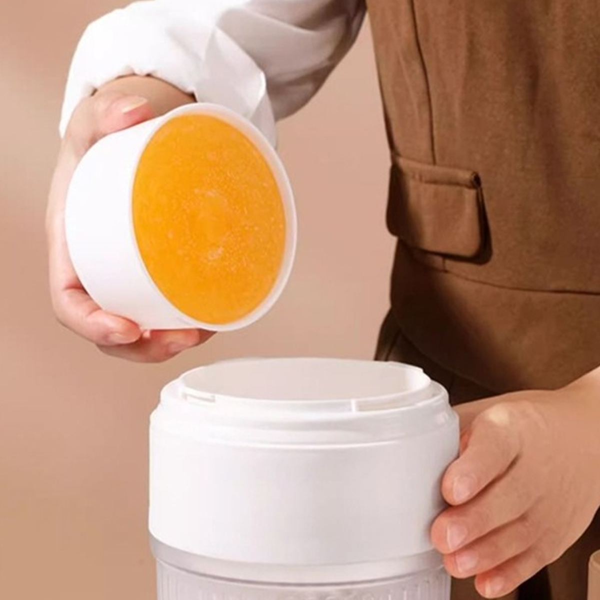 Eine Hand hält einen weißen Behälter mit einem orangen Eisblock.