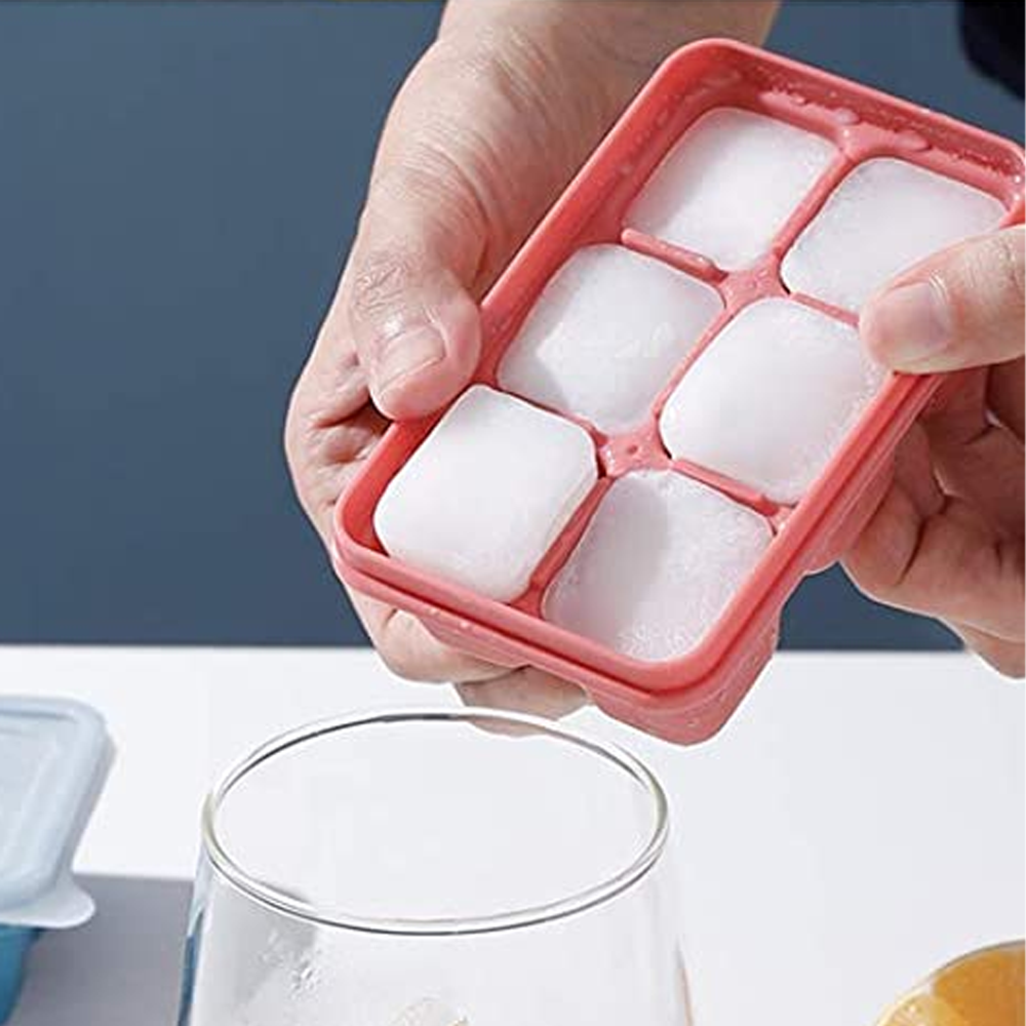 Eine Hand hält eine rosa Eiswürfelform mit Eiswürfeln über einem klaren Glas.