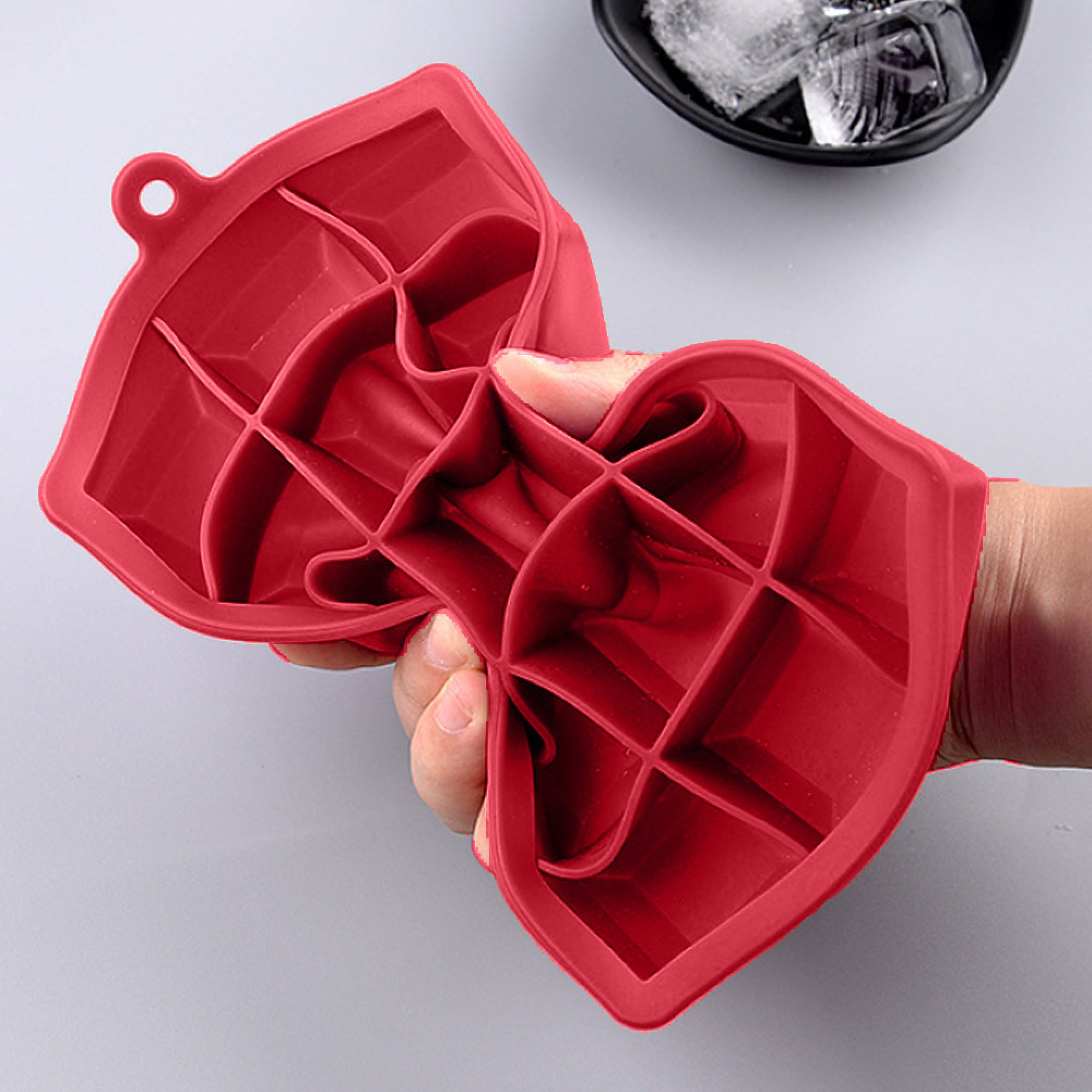 Eine rote Lippen-Eiswürfelform wird von einer Hand gehalten. Eiswürfel sind in einer Schüssel sichtbar.