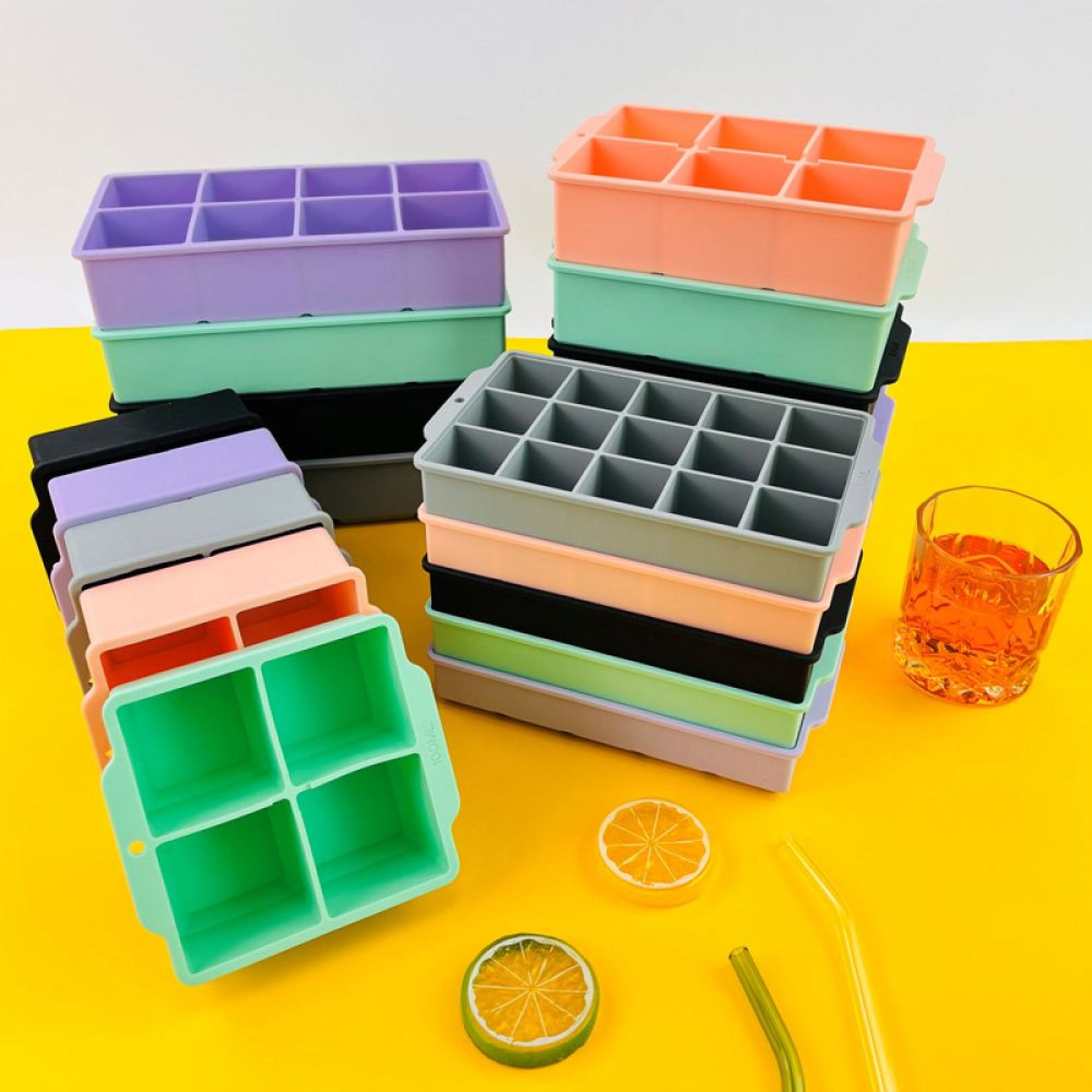 Bunte Eiswürfelformen stapeln sich neben einem Glas mit Getränk.