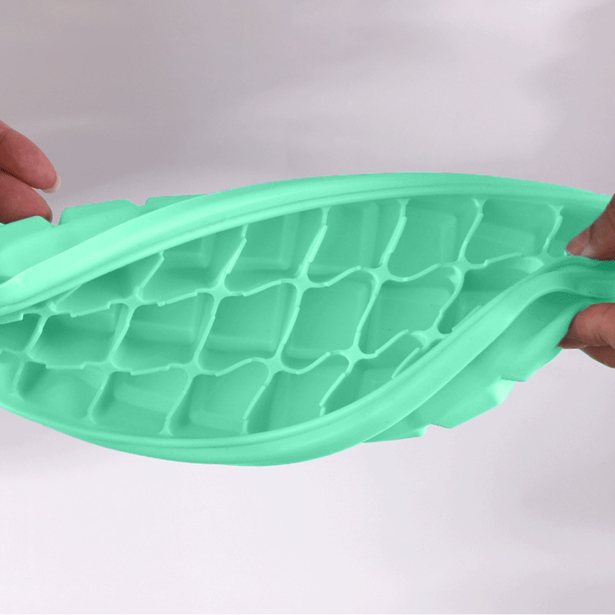 Hände biegen eine grüne Eiswürfelform mit vielen kleinen Quadraten.